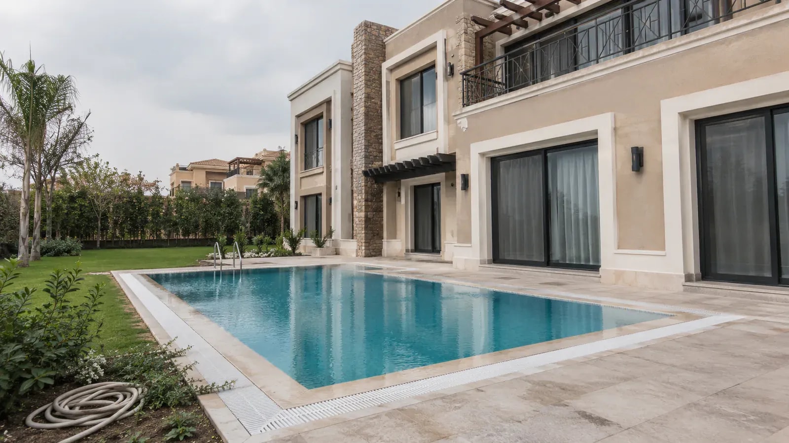 A rectangular pool beside a classic-style villa with a stone facade under an overcast sky
