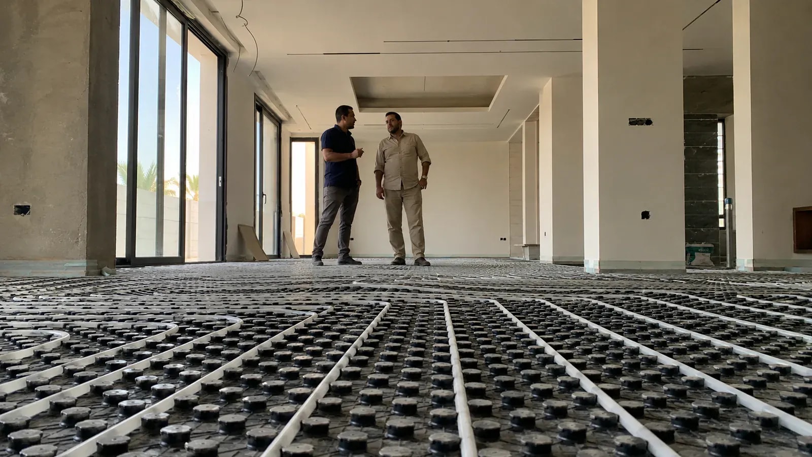 رجلان في صالة واسعة وأرضيتها بلوحات تثبيت سوداء لمواسير التدفئة