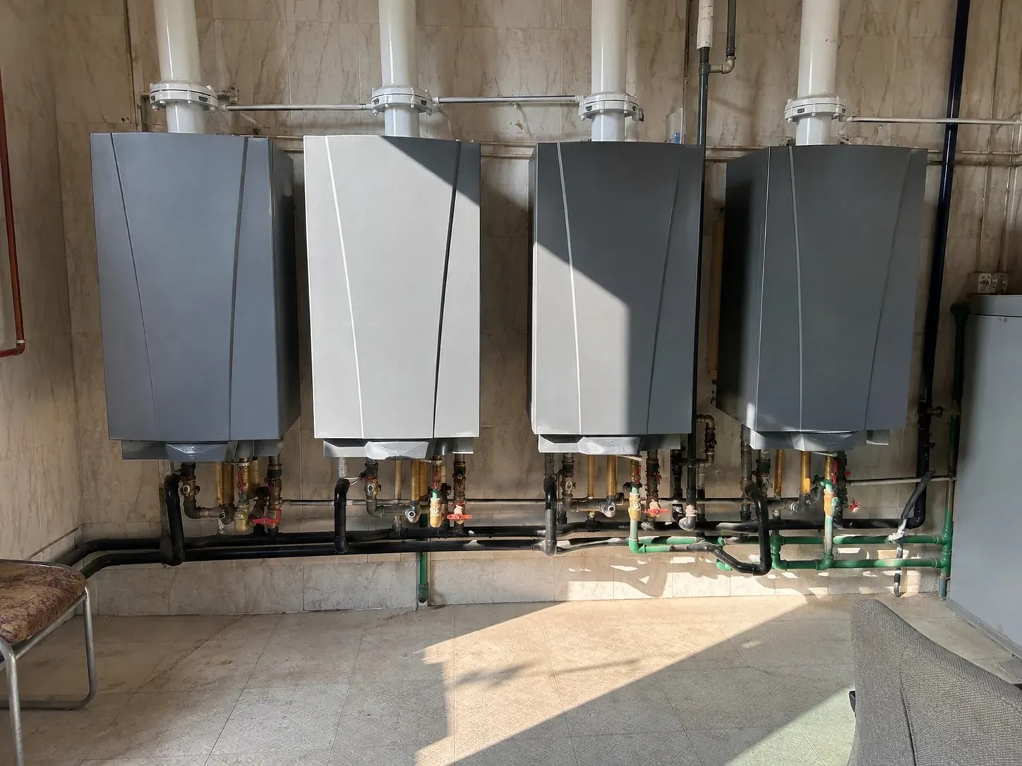 Four white wall-mounted gas boilers with tidy copper connections on a plant-room wall